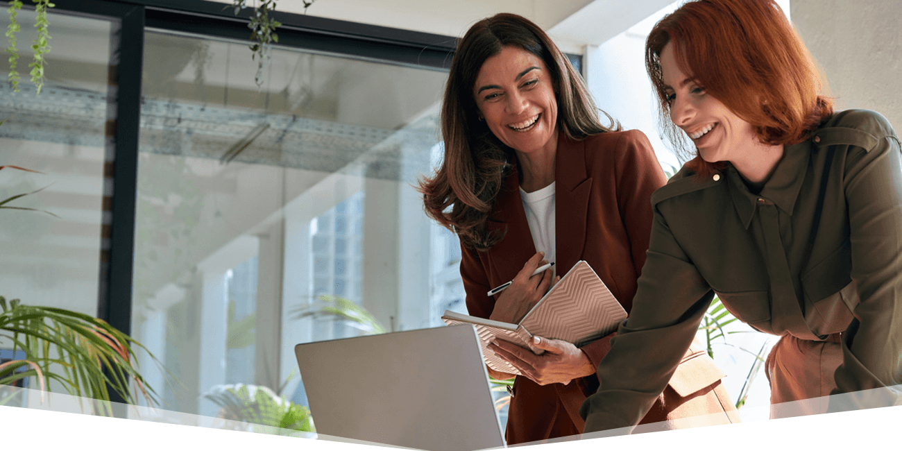 Two coworkers are smiling while looking down at a laptop